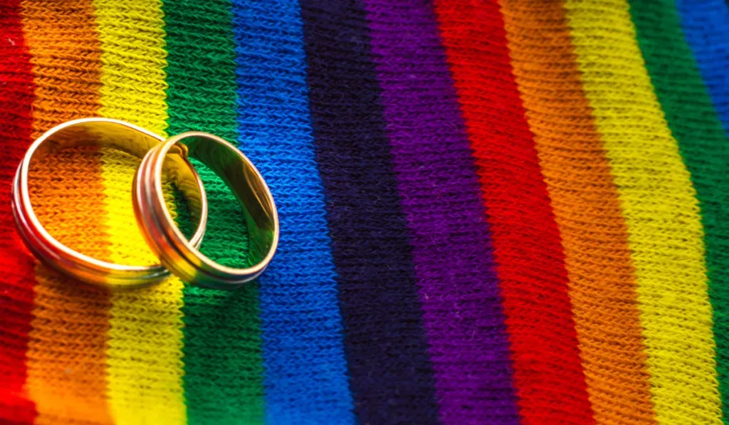 Two gold wedding rings resting on rainbow-striped fabric
